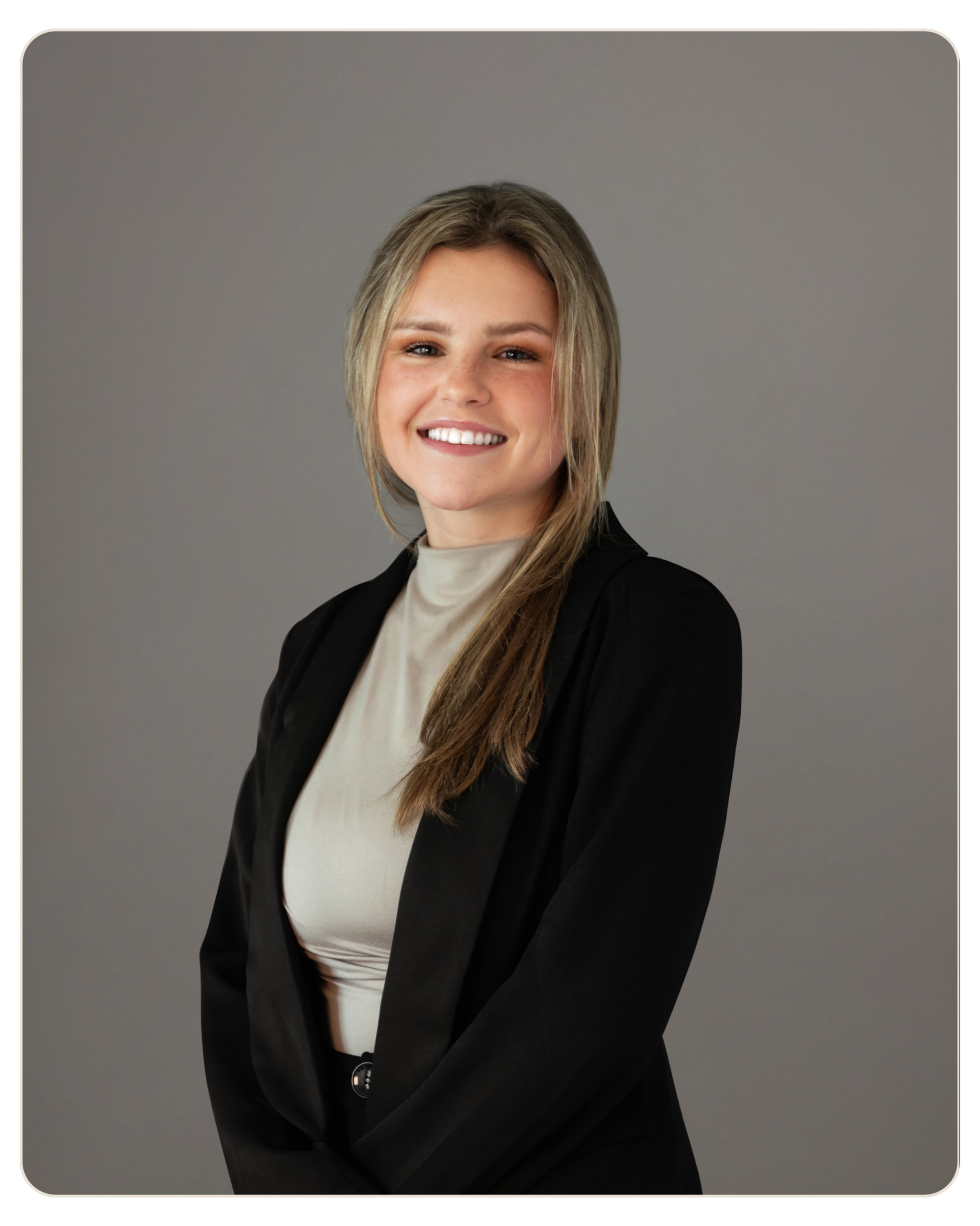 MaryJo Yarbrough Portrait of a smiling blonde woman in a black blazer and beige blouse, arms crossed, against a gray studio backdrop.