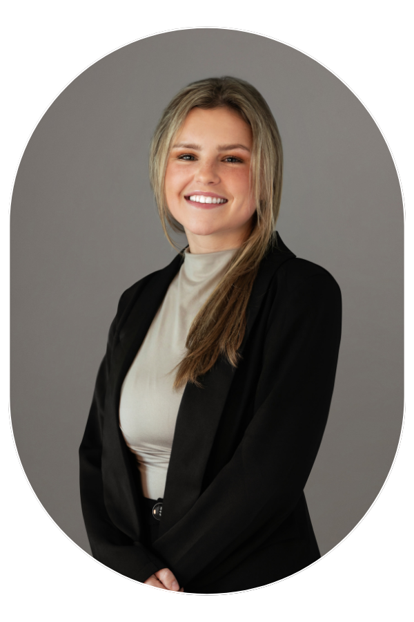 Professional headshot of a smiling woman in a beige top and black blazer against a gray background.